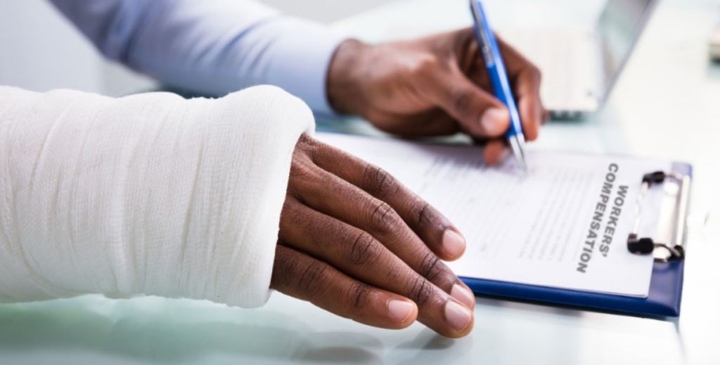 Photo of a person with a wrist cast signing a worker's compensation form