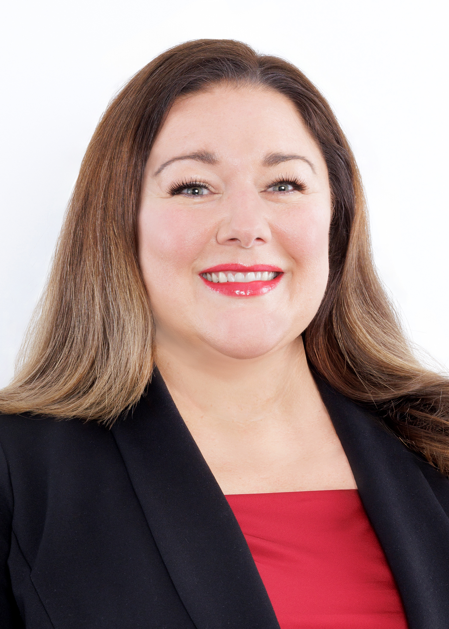 Smiling woman with long brown hair wearing a black blazer and red top, photographed against a plain white background.